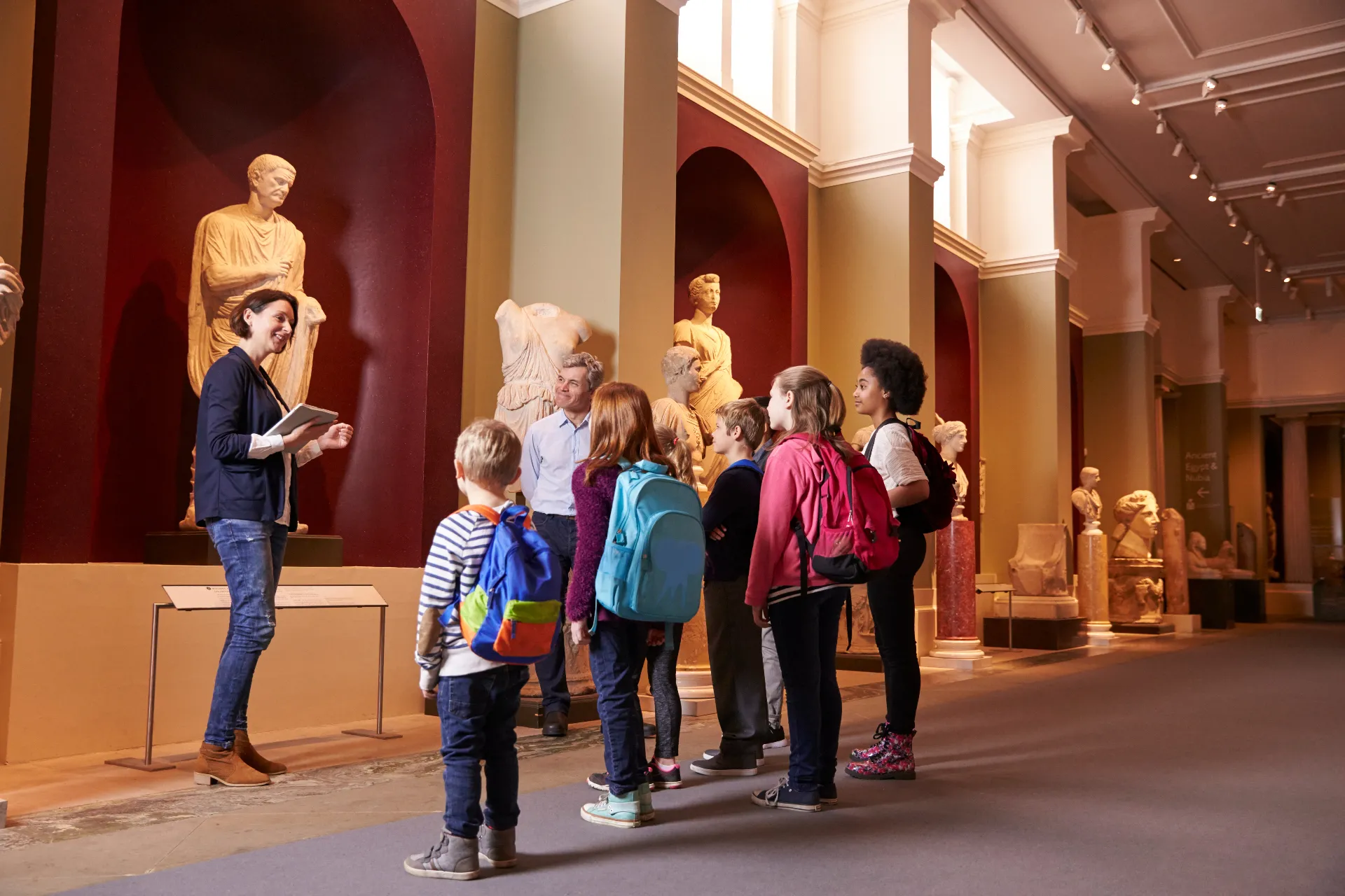 Eine Gruppe Schulkinder mit Lehrerin betrachten eine Statue